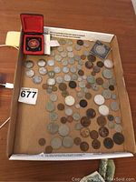 Wide view of the collection showing coins spread out in a cardboard box with two coins in protective cases and stacked paper notes.
