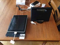 Apple iPad lying flat with charging cable connected, with Sony audio dock unit next to it on wooden table.