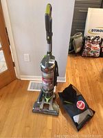 Full view of the upright Hoover vacuum cleaner with its accessory bag on the floor beside it, showing the overall design and color scheme.