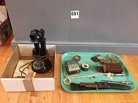 Antique telephone in a cardboard box with various small items laid out on a blue tray, including knife, compass, pillboxes, and jewellery box.