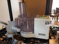 Braun Multipractic Plus food processor main unit and bowl with lid and attachments visible on nearby surface.