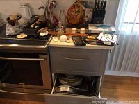 Overall kitchen counter showing assortment of utensils, knife block, digital scale, trays, and miscellaneous small kitchen items