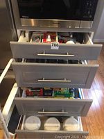 Kitchen drawers open showing organized kitchen items including food wraps, plastic storage containers, tins, and canisters.