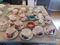Overview showing multiple assorted bone china tea cups and saucers with floral patterns, plus two creamers and a sugar bowl