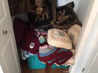 Crocheted pillows and folded afghans in a closet with plastic totes underneath