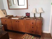 Full view of teak styled wooden dresser with six drawers, two doors, and wood framed mirror above it.