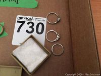 Three white gold rings on cardboard with MaxSold tag: plain band, multi-prong setting, solitaire-style setting