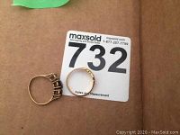 Both gold rings displayed on cardboard backing, one plain three-prong mount and one intact red-stone ring