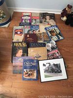 Overview photo of entire collection showing books, magazines, mugs, and framed print laid out on a floor.