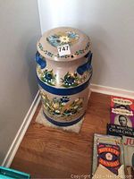 Front view of decorative painted milk can resting on a small rug on wood floor with books next to it.
