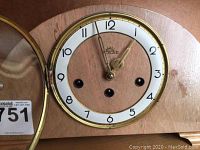 Close-up photo of Solar clock face showing white dial with gold trim, black numbers, and three winding holes.