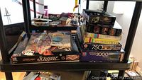 Scrabble board game box and multiple jigsaw puzzles stacked on a table.
