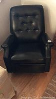 Front view of black pleather rocker recliner with button tufted backrest and padded arms.
