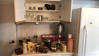Photo showing various barware, glasses, pitchers in cabinet and on shelf with accessories on counter below