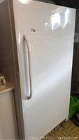 Angled front view of white upright freezer showing exterior condition and handle