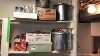 Wide shot of shelves with large pot with lid and handles, multiple jars in cardboard trays and bins, and boxes of Bernardin lids