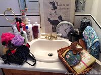 Bathroom sink with assorted toiletries, loofahs, hair dryer, framed print, and clock.