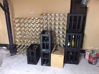 Photo showing two wooden wine racks, light wood color, with slot compartments for bottles, alongside black plastic wine crates with some wine bottles inside.
