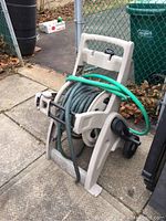 Front-side view of mobile hose reel showing beige plastic frame, black wheels, and coiled green hose.