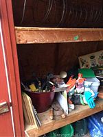 Full view of garden hand tools, gloves in package, a wooden-handled tool, and decorative lawn ornament stored on shelves in a shed.