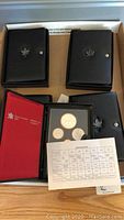 Five black Royal Canadian Mint coin presentation cases, one open showing interior case, arranged on table