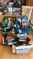 Overview of assorted household items including painting supplies, slippers, clothing, tools and others on wooden floor.