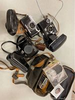 Top view of three 35mm cameras with their cases and a zippered pouch holding accessories and film.
