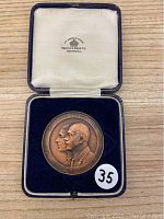 Front of the bronze medal showing profiles and inscriptions inside a blue velvet box.