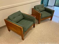 Front view of two teak framed chairs with green cushions on a tiled floor near window
