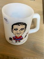 Full view of milk glass mug with caricature of Frank Mahovlich in Canadiens hockey uniform and dog.