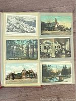 Photo of an open album page showing six postcards including prominent buildings, forest, and street scenes