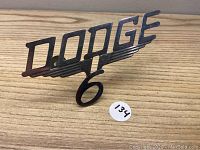 Front view of vintage Dodge V8 6 metal emblem showing design details and condition.