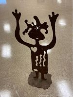 Full front view of handmade metal sculpture showing stylized human figure with raised arms standing on flat base.