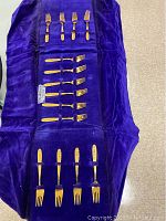 Purple velvet soft case open displaying rows of gold-tone forks