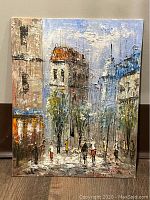 Front view of oil painting showing street with pedestrians and buildings, signed in red at lower right.