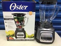 Oster power blender with glass jar, lid, control panel and box showing brand and Duralast series details.