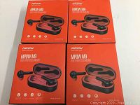 Four unopened boxes of Mpow M9 true wireless earbuds with charging cases shown in orange retail packaging.