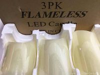 Three cream-colored flameless LED candles in white protective Styrofoam packaging inside an open box labeled '3PK FLAMELESS LED Candle'. Candles have smooth cylindrical shapes with flat bottoms showing battery compartments and switches.