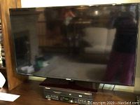 Front view of Samsung flatscreen TV on its pedestal stand with VCR/DVD combo visible beneath