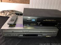 JVC VHS VCR stacked on silver Sony DVD player, with remote control on JVC unit.