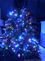 Artificial Christmas tree lit with multicolor string lights in a dim setting.