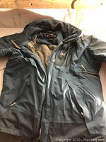 Photo showing the full grey winter jacket with beige padded interior and multiple zippered pockets.