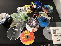 Photo showing a Panasonic Lumix blue digital camera, Rubik's Cube, multiple DVD and CD discs scattered on black surface.