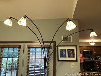 Full view of the floor lamp with five arched arms each topped with a Tiffany-style stained glass shade against a living room wall.