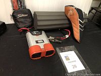 Gray foam roller behind Black & Decker power converter, Titleist bag on left, Big Bertha head cover on right, golf tees in front