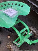 Side view of the green garden tractor scooter showing perforated metal seat and sturdy tubular frame with small knobby tires.