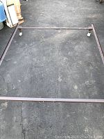 Rectangular metal queen-size bed frame on concrete floor with caster wheels visible. Frame is in solid condition with minimal wear.