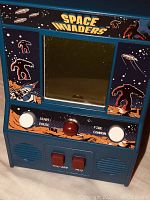 Front view of the Space Invaders portable game showing screen, buttons, and artwork