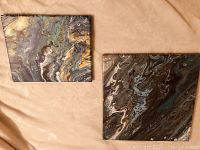Both square abstract fluid art paintings shown side by side on beige fabric.