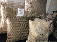 Queen size comforter with multiple decorative pillows in beige and gold tones packed and displayed, showing texture and pattern detail.